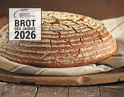 Ein Altfränkischer Roggenlaib liegt auf einem Holzbrett, darunter ein beiges Leinentuch